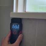 Moisture meter picking up water content behind a shower tile wall